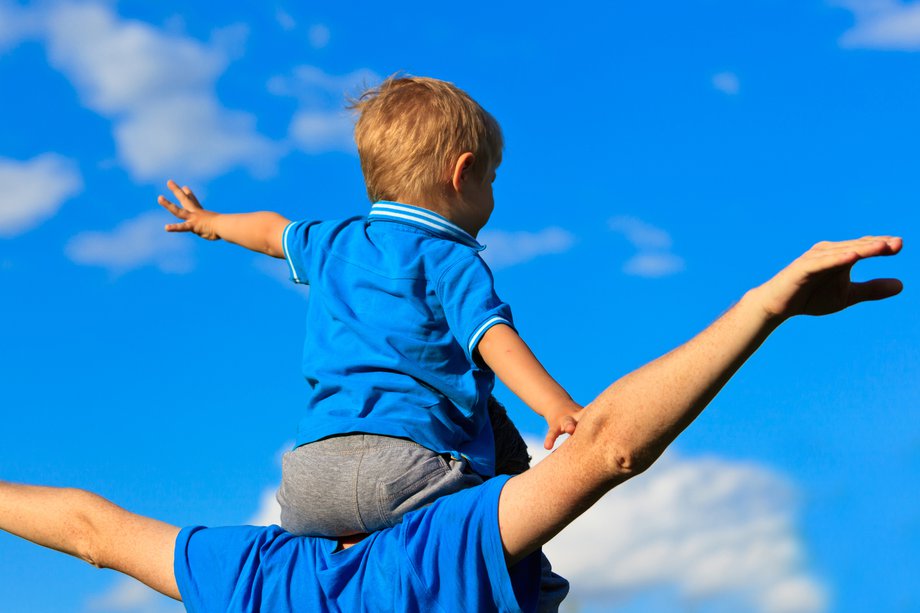 A young child sitting on the shoulders of an adult – both's arms are outstretched