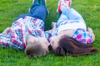 A teen boy and girl lying on grass gently touching their noses together